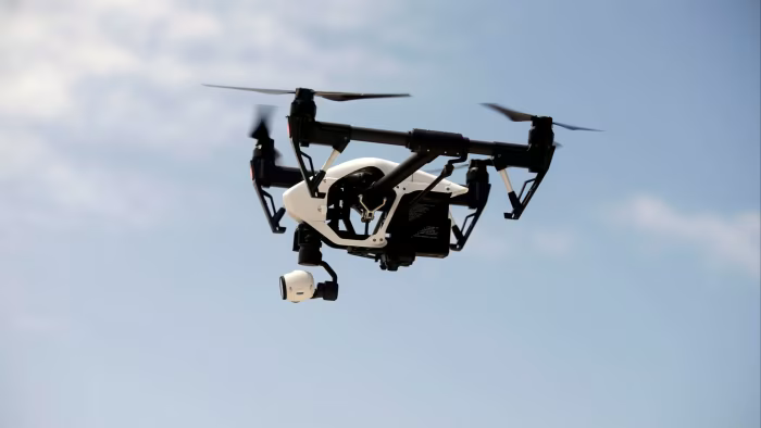 A DJI Inspire drone with a white body and black propellers hovers in the sky