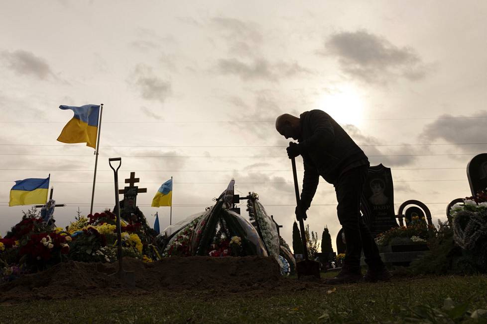 Venäjän hyökkäyssodassa kaatuneiden ukrainalaissotilaiden hautoja Butšan hautausmaalla numero 3. Haudankaivaja lapioimassa hautaa umpeen lokakuussa 2022.