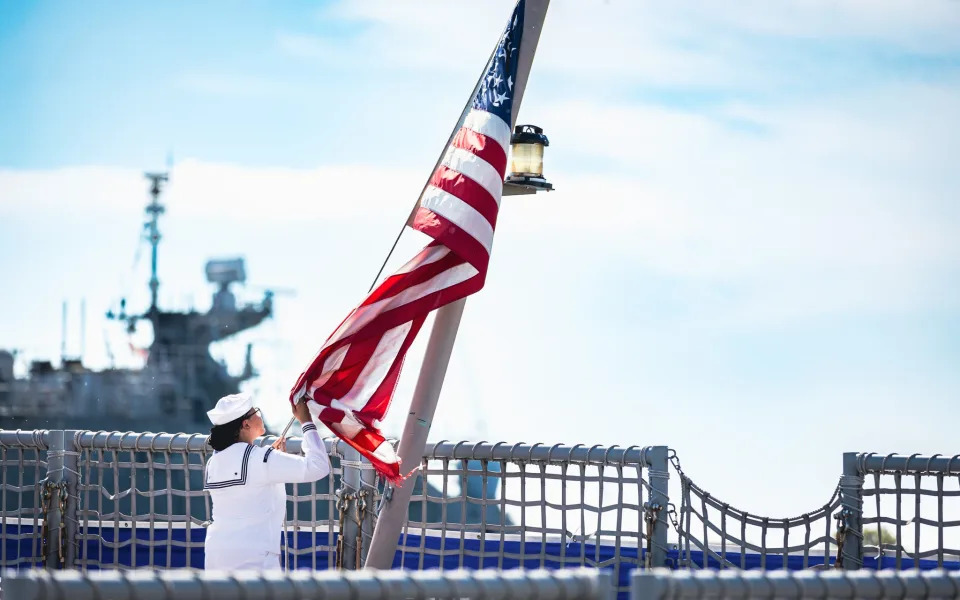 A Sailor assigned to the USS Sioux City (LCS 11), takes down the ensign for the final time during a decommissioning ceremony for the ship at Naval Station Mayport, Aug. 14, 2023.