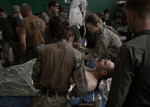 A soldier lies on a stretcher bed with medics in military fatigues in attendance.