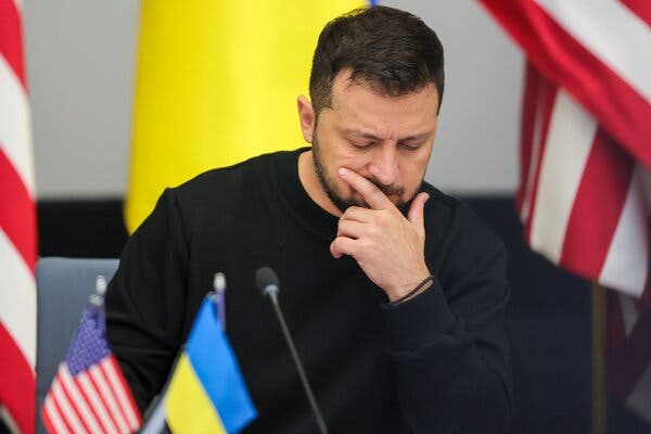 President Volodymyr Zelensky in a dark sweater. His hand is near his mouth.