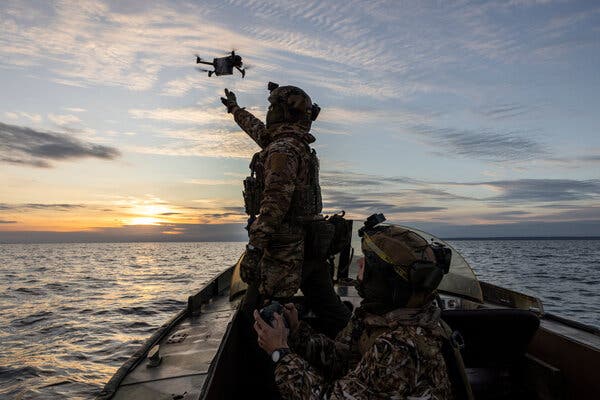 Two Ukrainian soldiers in a boat launch a small drone as the sun sets over the water.