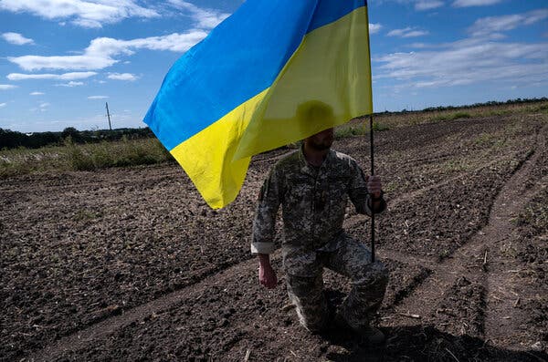 A soldier holding a blue and yellow Ukrainian flag.