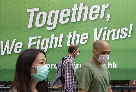 Hengityssuojaimin varustautuneet hongkongilaiset kulkivat koronavirusaiheisen julisteen ohi sunnuntaina.