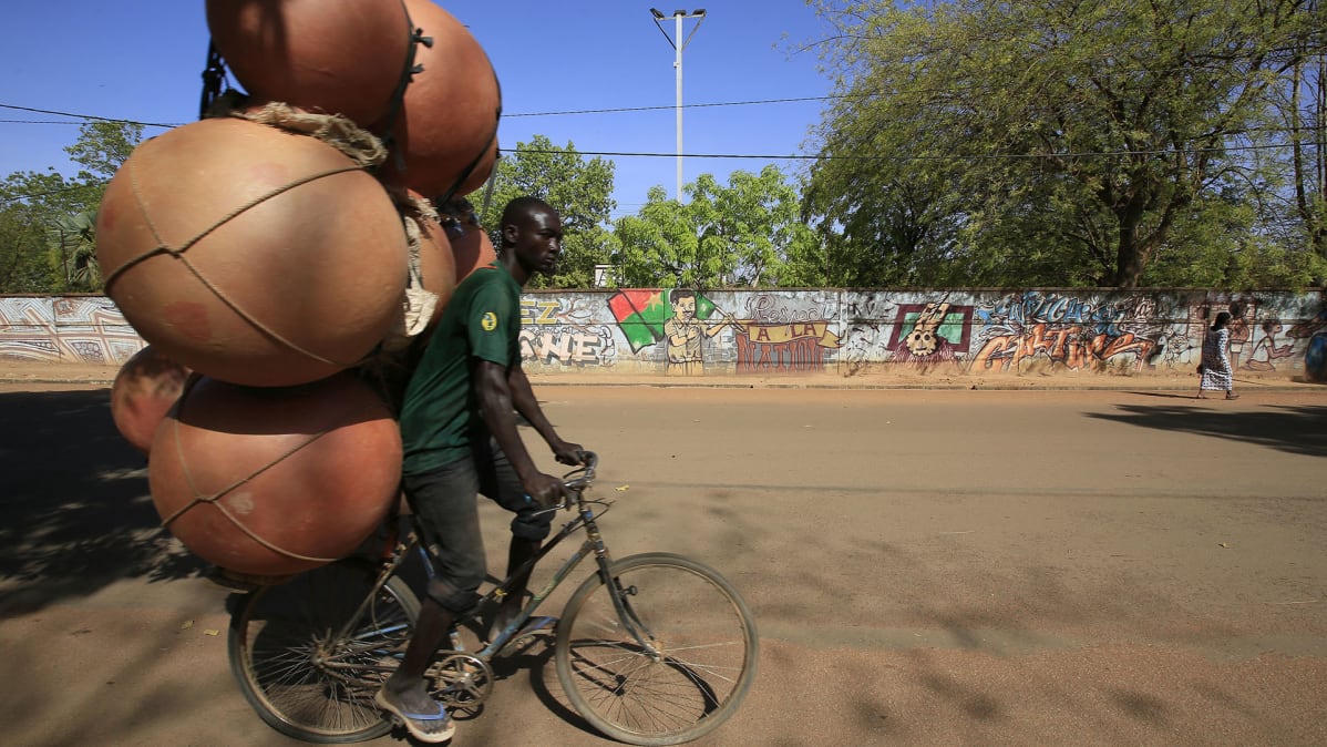 Mies pyöräilee kyydissään säiliöitä Ouagadougoussa, Burkina Fasossa.