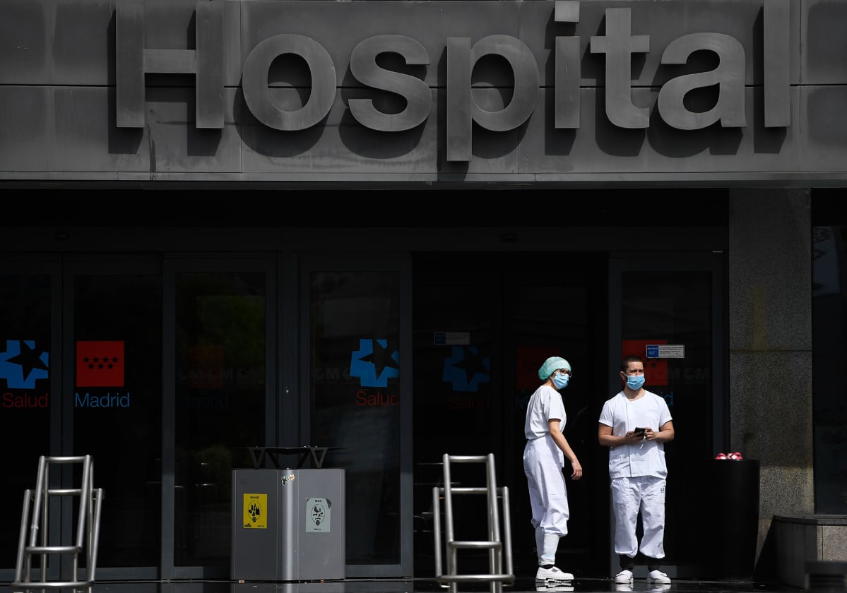 Kaksi hoitohenkilöstöön kuuluvaa seisoo sairaalan edustalla Madridissa.