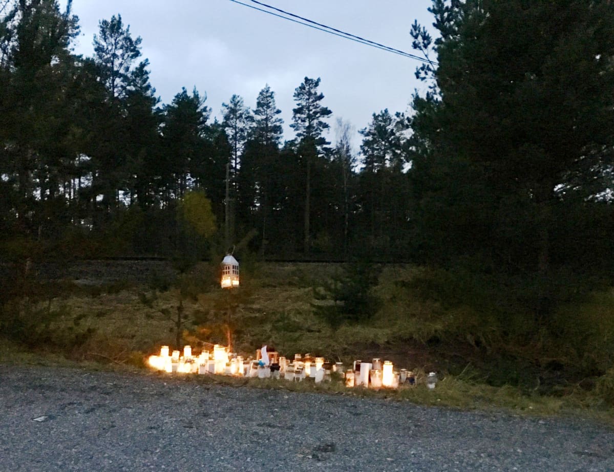 Många ljus brinner på marken vid en plankorsning till minne för fyra personer som avled i en olycka i slutet av oktober 2017.
