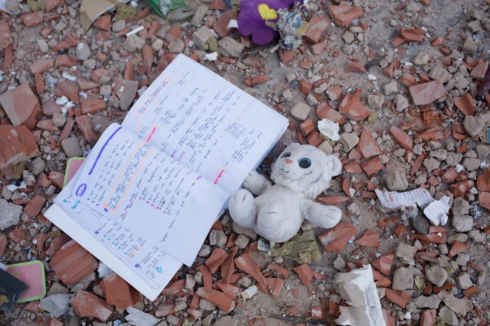 A toy and a notebook lie among crumbled bricks and other debris. A toy and a notebook lie among crumbled bricks and other debris.