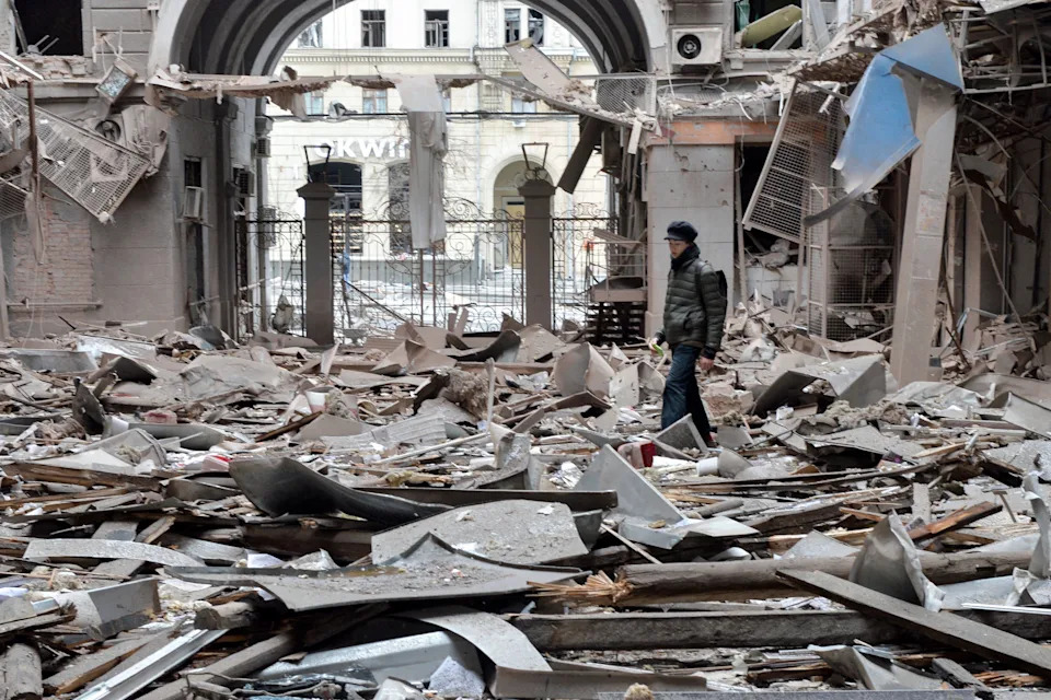 A view from inside of a heavily damaged building, with someone wearing all black standing amid the debris. A view from inside of a heavily damaged building, with someone wearing all black standing amid the debris.