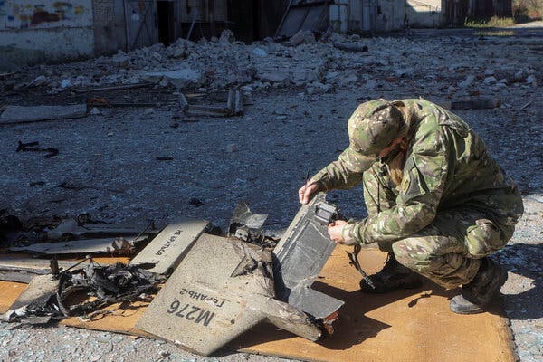 An individual in military uniform inspecting pieces of a drone amid rubble.